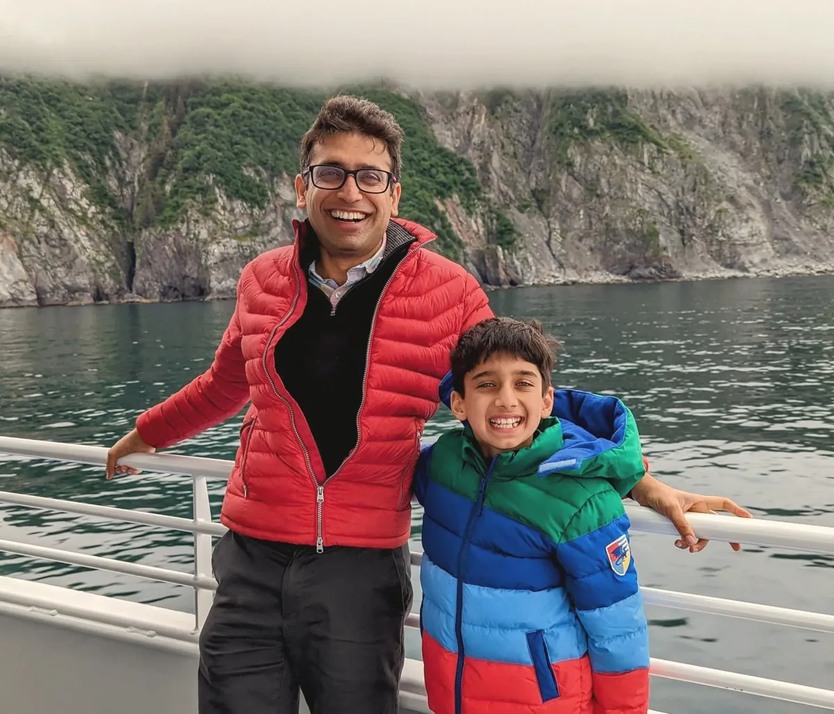Sameer Vermani with his son, smiling on a boat before misty cliffs and water