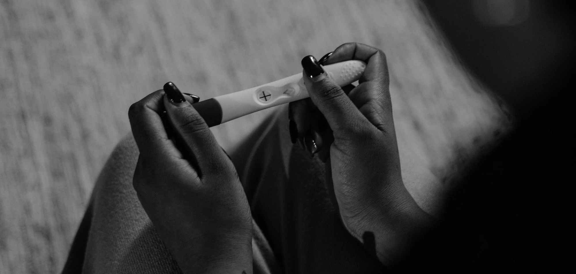 A woman sitting alone, holding a home pregnancy test
