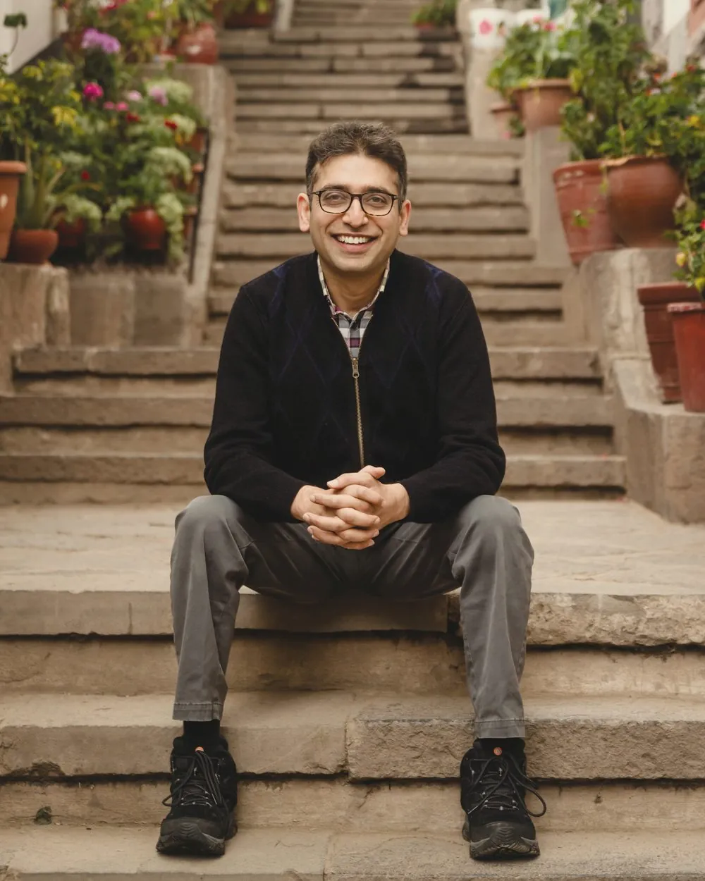 Sameer Vermani seated on stone steps, smiling, potted plants behind him