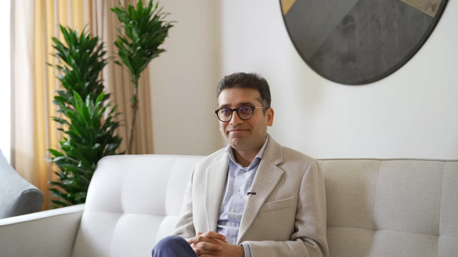 Sameer Vermani seated on a sofa, speaking to camera in The Invisible Cure