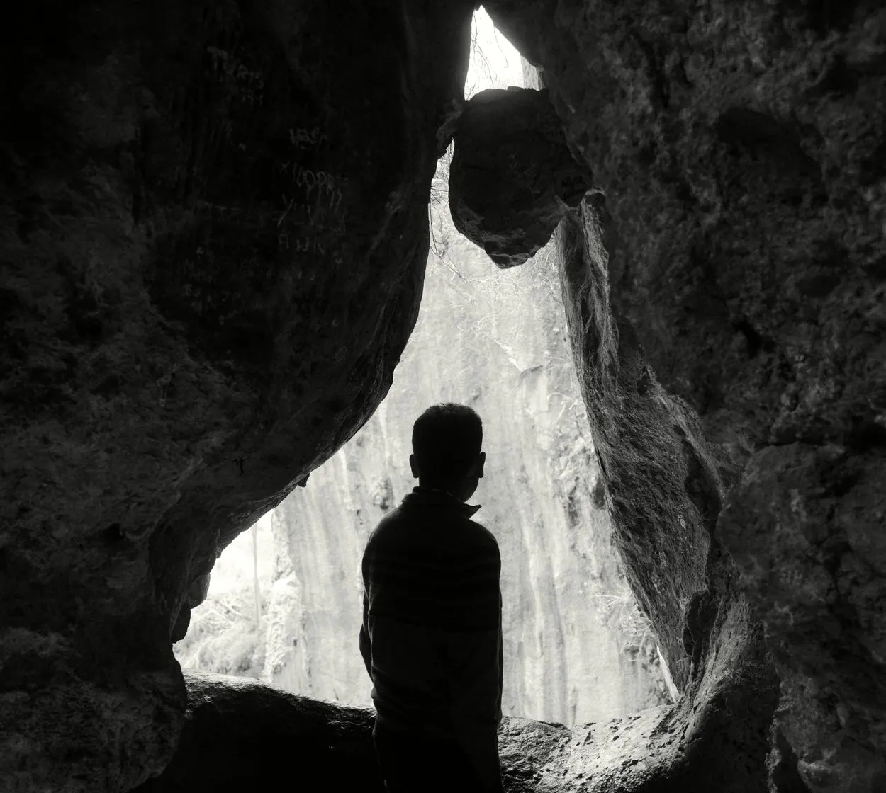 A lone figure in silhouette looking toward light at the mouth of a cave